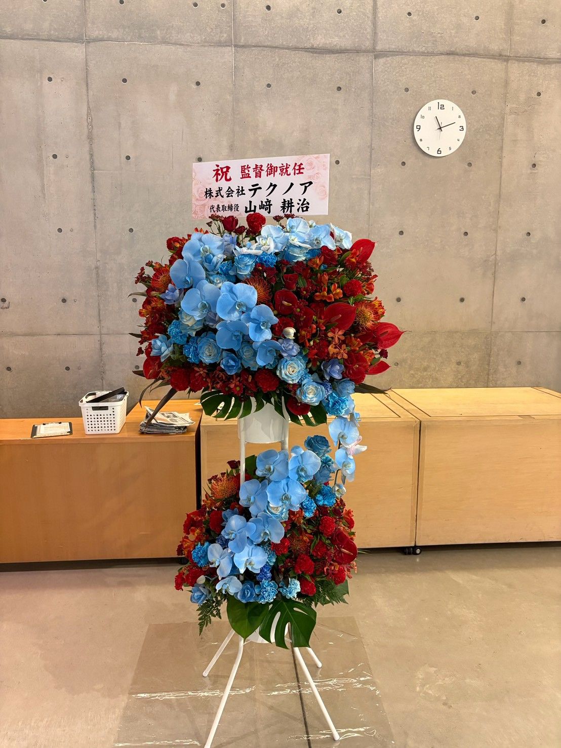 「祝 監督御就任」の札が付いた、青と赤の花のスタンド