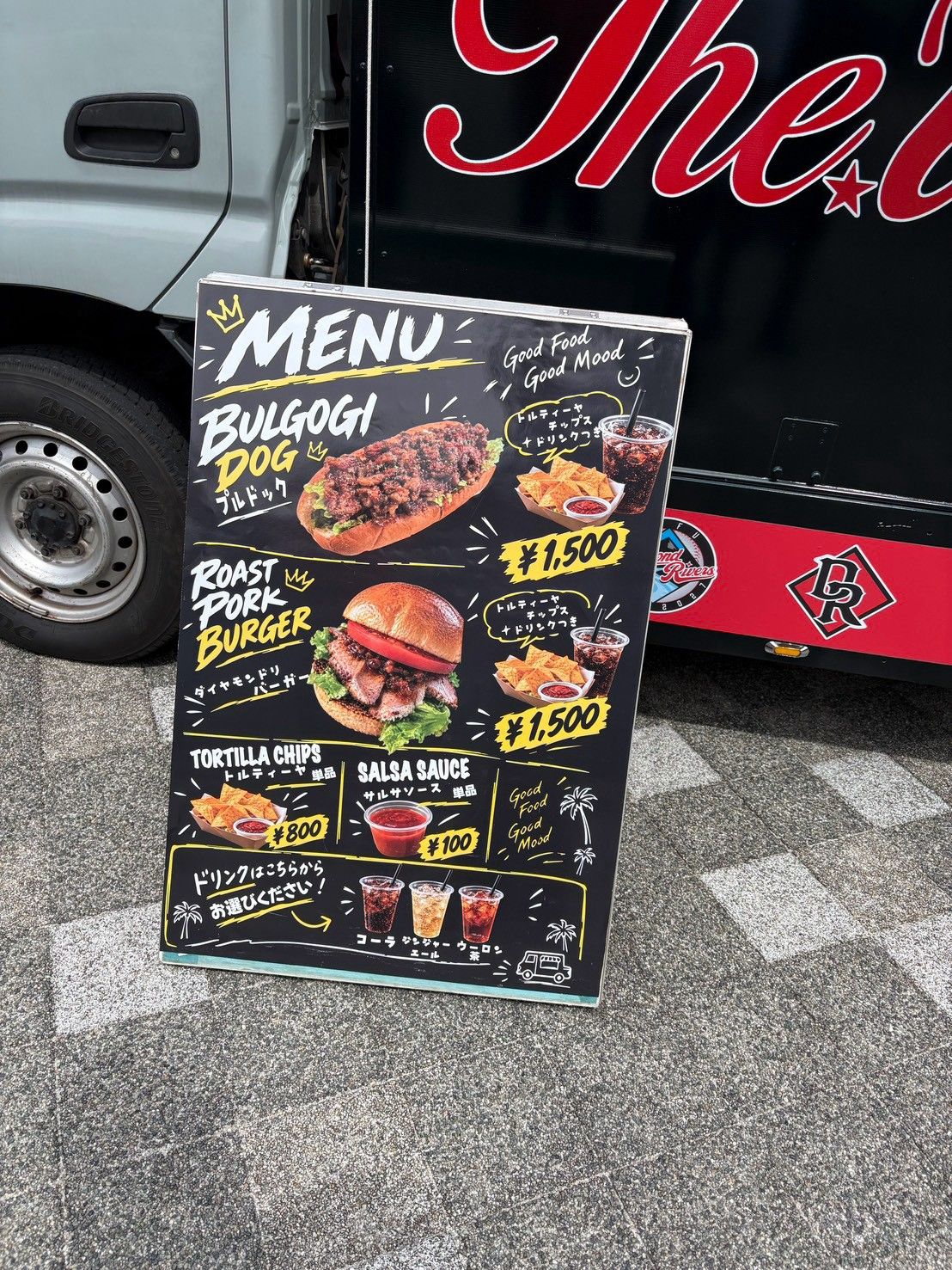 キッチンカーの前に立てられたメニューボード。プルコギドッグやローストポークバーガーの写真