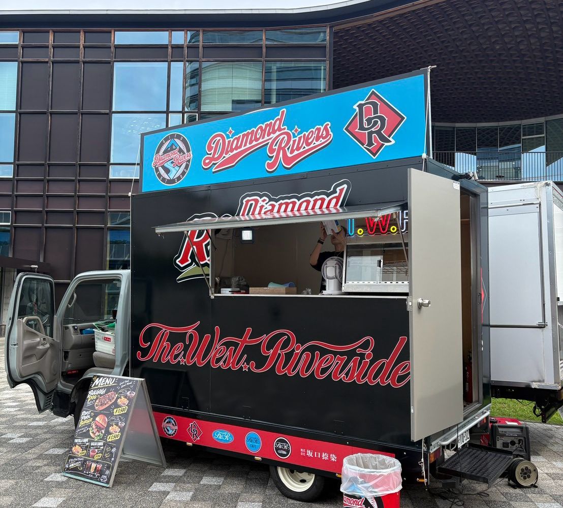 ぎふメディアコスモスの前に停まる球団公式キッチンカー。青い看板に「Diamond Rivers」のロゴと「DR」マーク