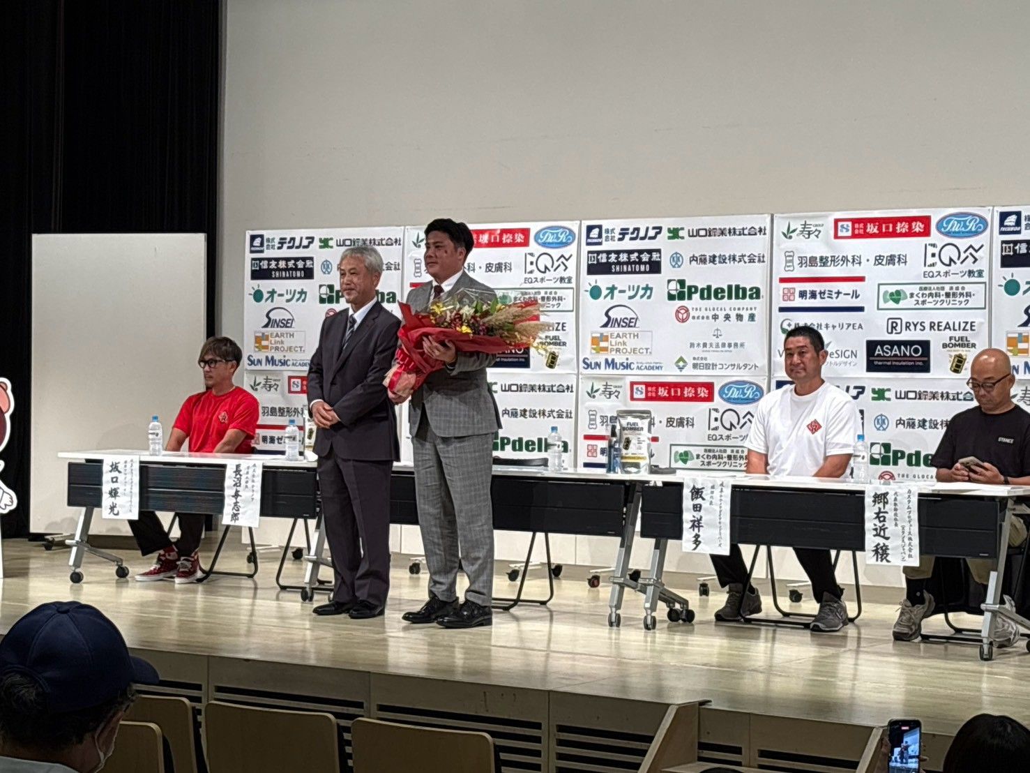 就任会見のステージで花束を受け取った若松駿太監督(右)と来賓
